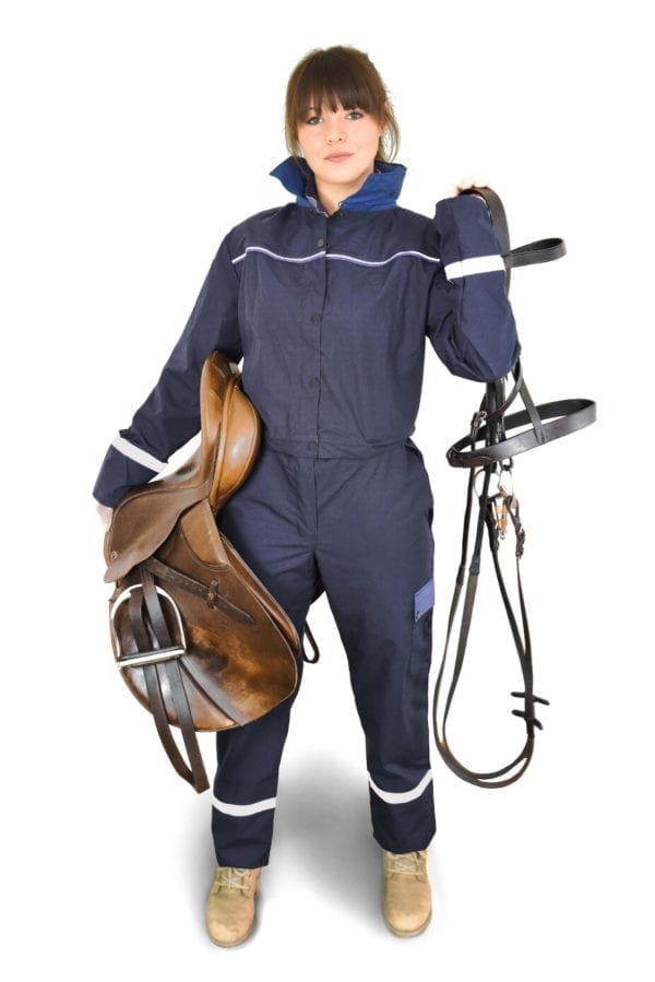 a girl wearing classic blue coverall holding horse saddle and climbing harness