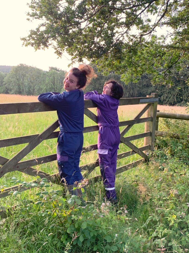 Two ladies wearing 3- Donkeys women's coveralls in long grass and woodland.