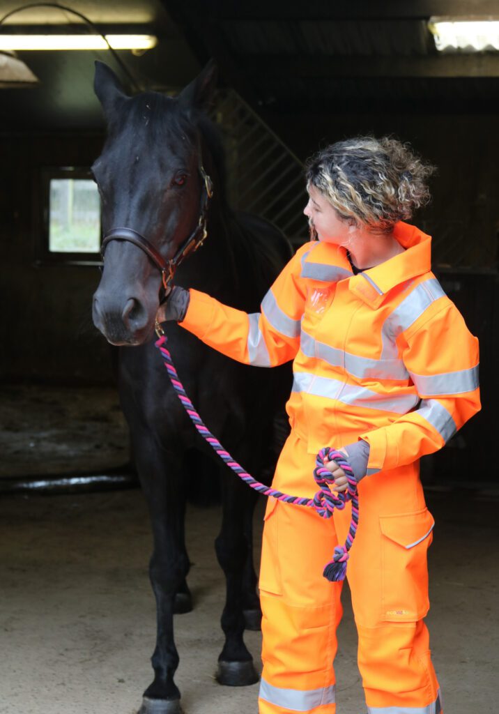 Model wearing 3 Donkeys Exmoor Coveralls in hi-vis orange with horse.